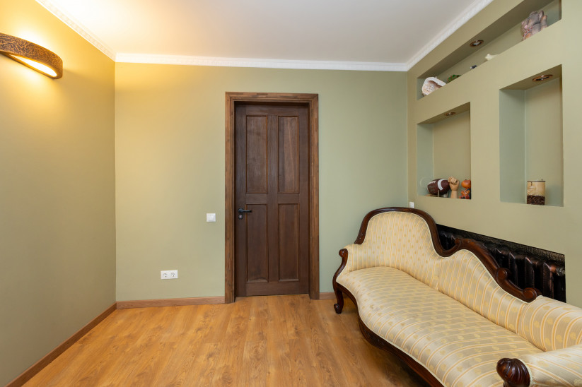 Dzeltena antīka sofa zaļā istabā.