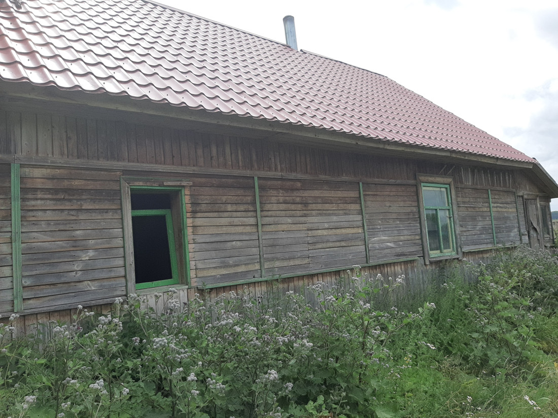 Koka māja ar sarkanu jumtu laukos.