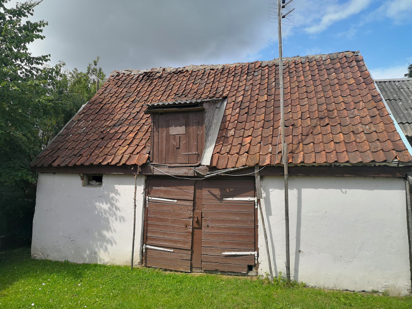 Veca šķūņa fasāde ar sarkanu jumtu.