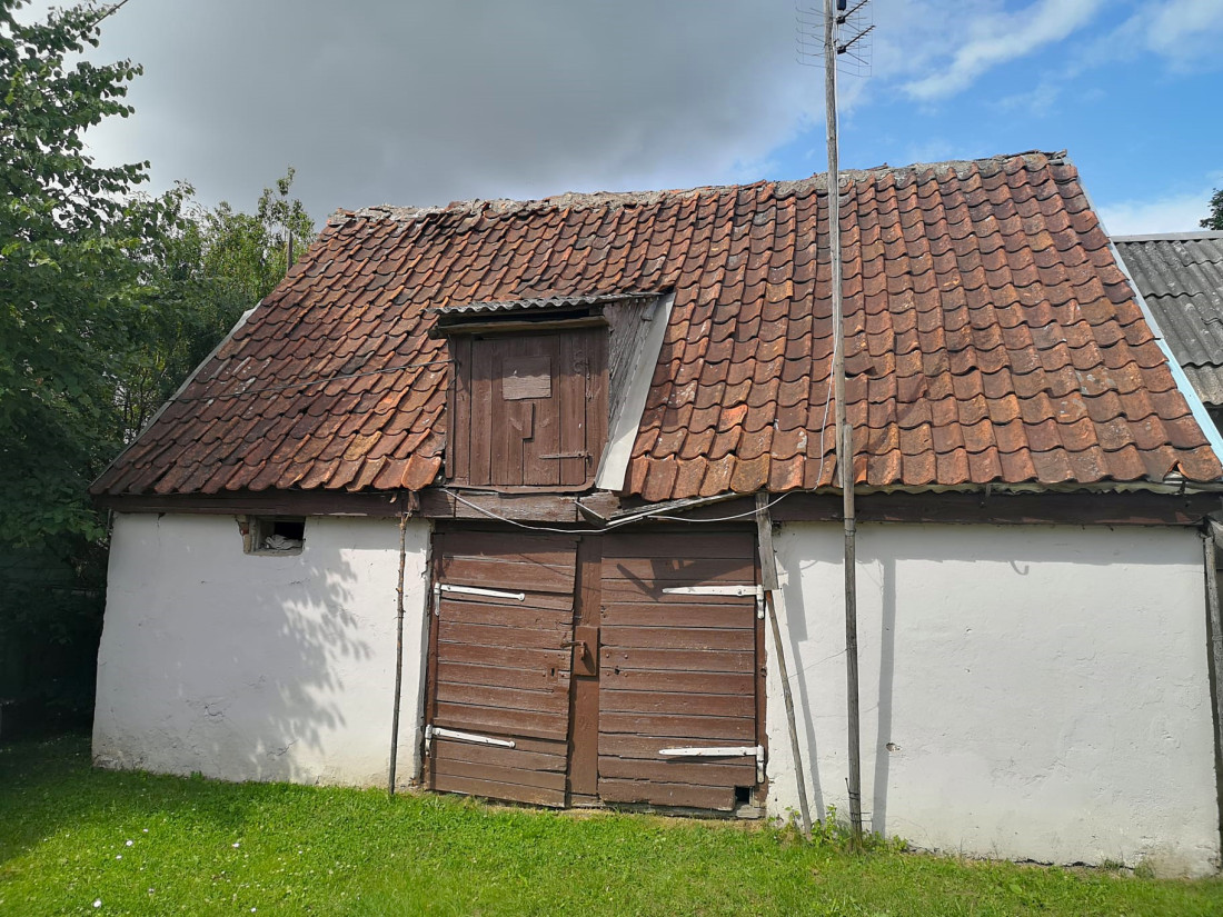 Veca šķūņa fasāde ar sarkanu jumtu.