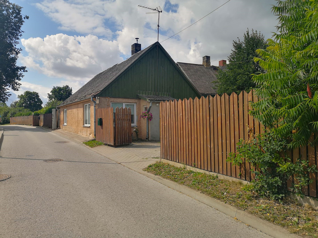 Māja ar zaļu koka fasādi un sētu.