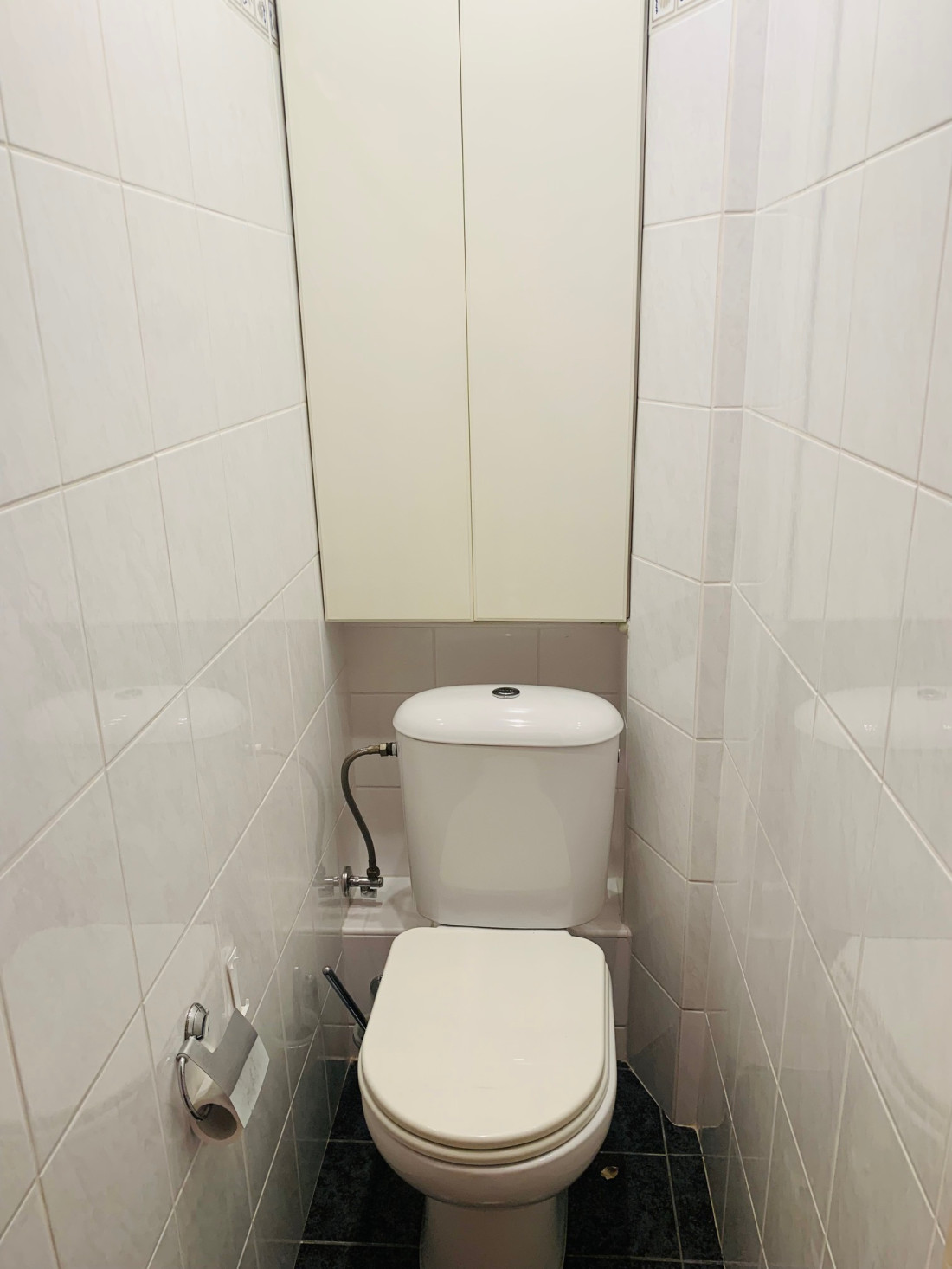 Narrow toilet view with cabinet.