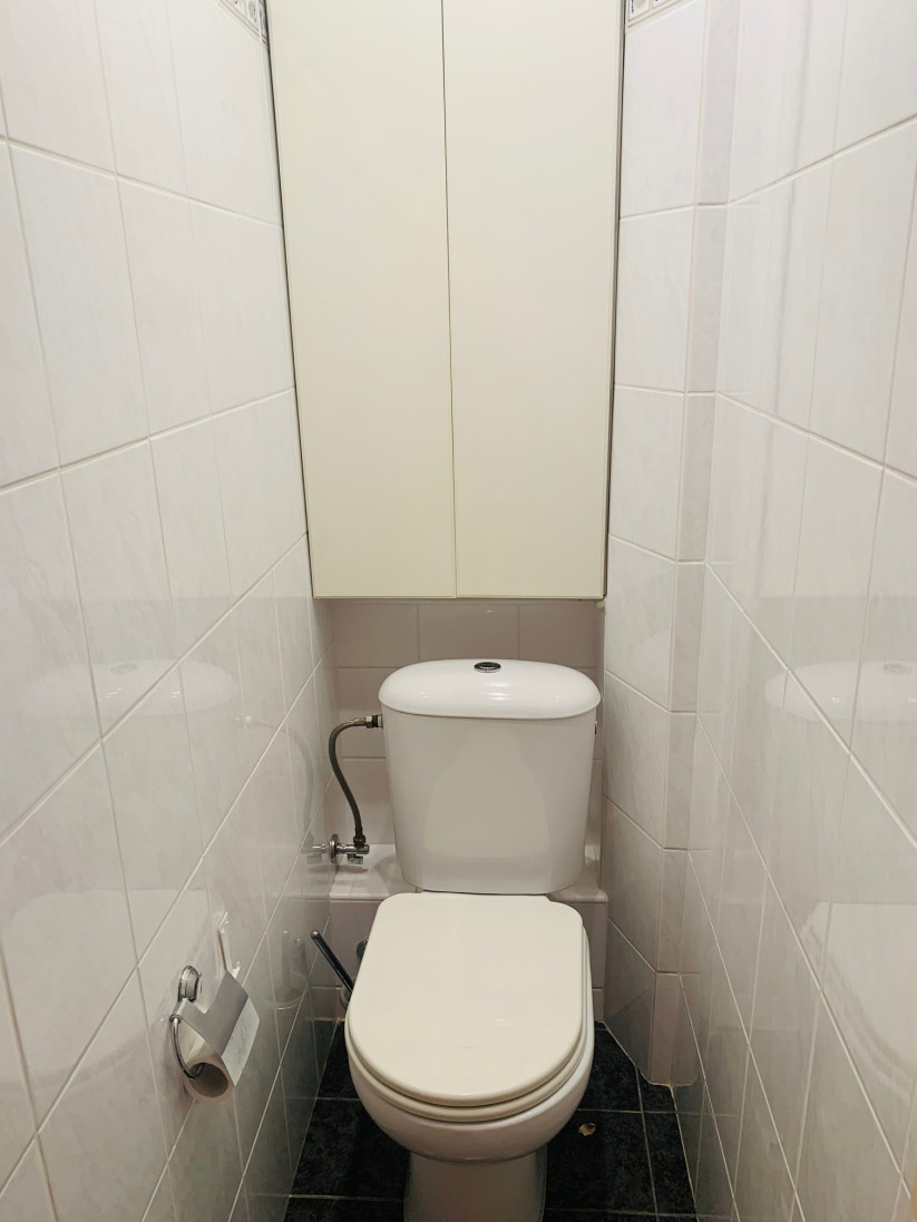 Narrow toilet view with cabinet.