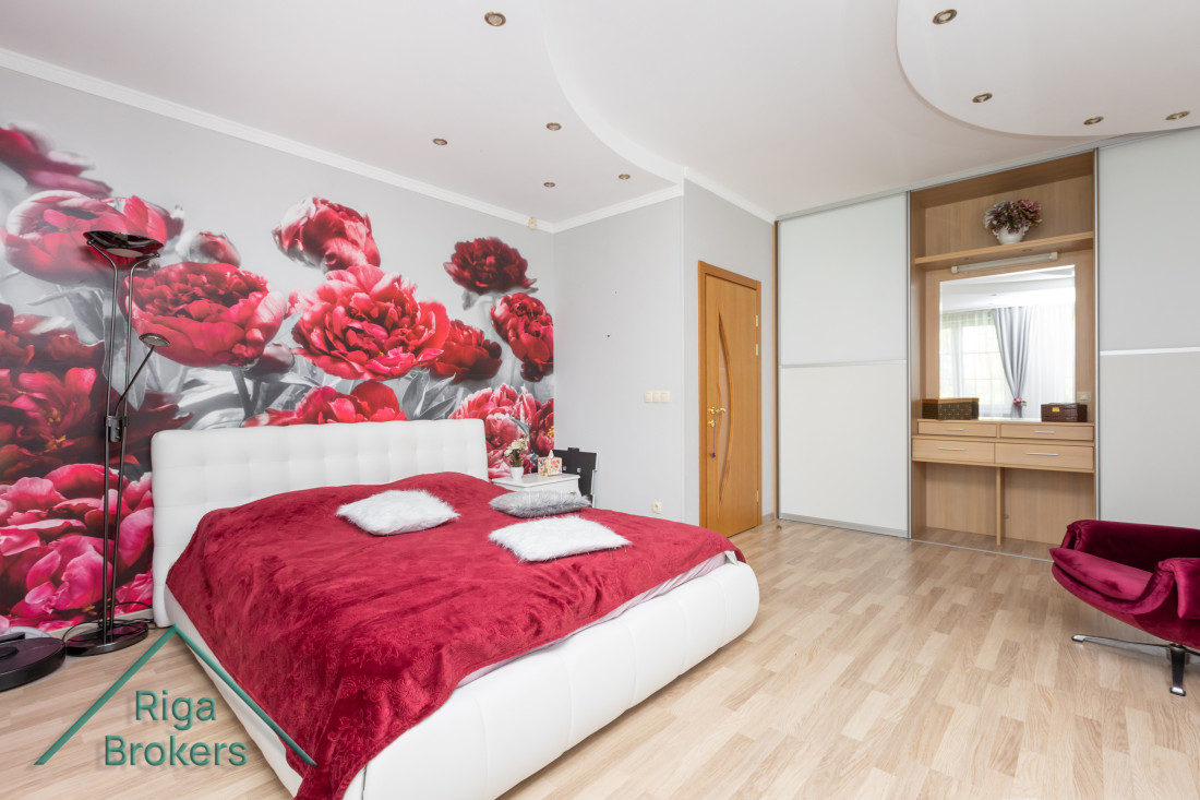 Bedroom with red bedspread and floral wallpaper.