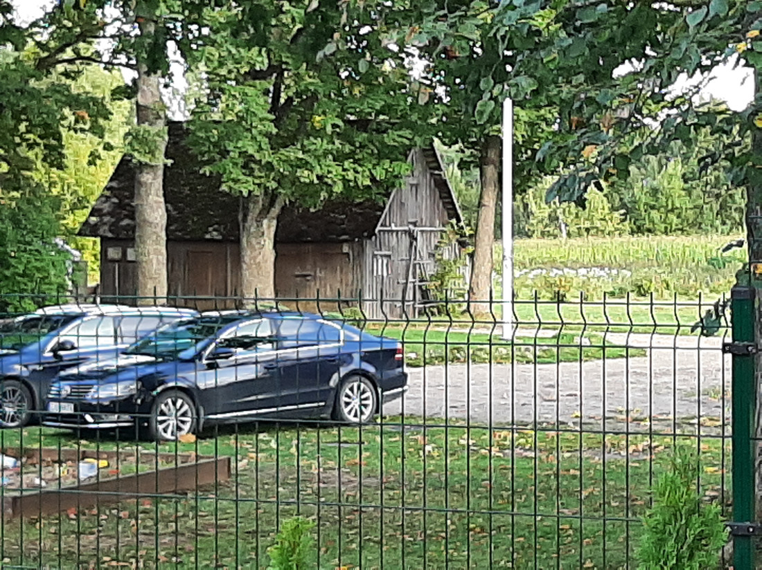 Auto stāvlaukums pie koka šķūņa.