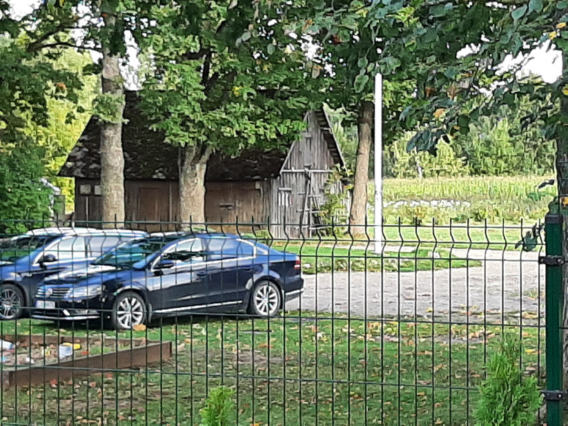 Auto stāvlaukums pie koka šķūņa.