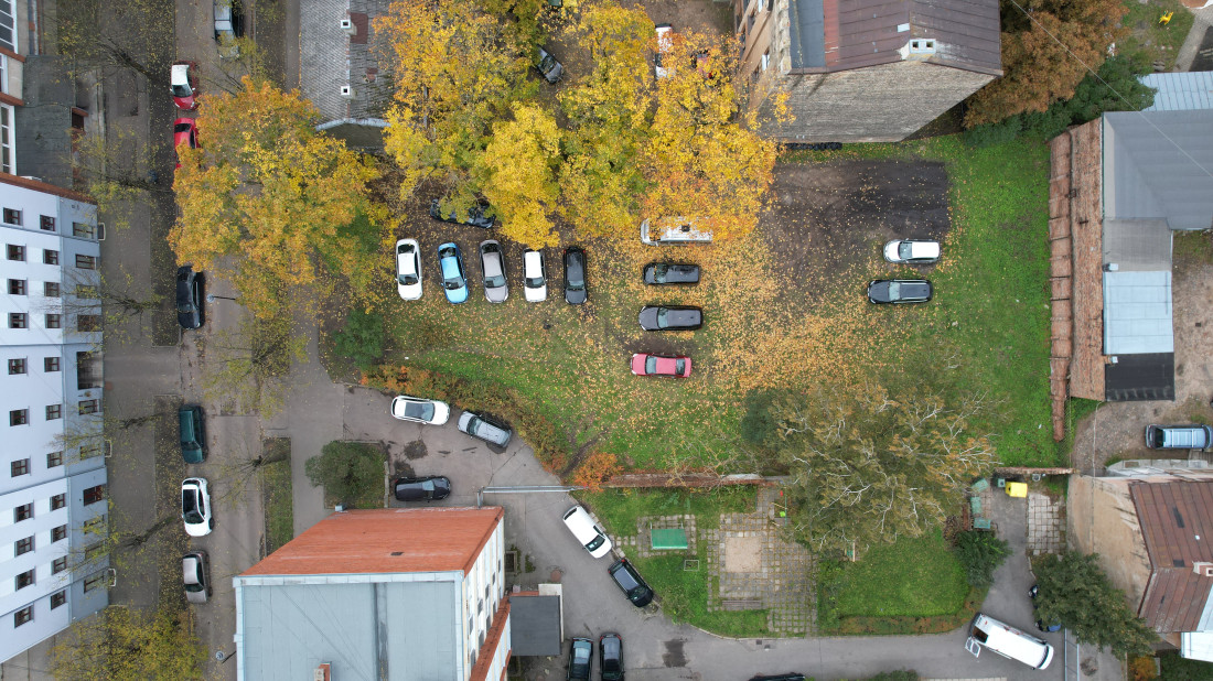 Autostāvvieta starp mājām ar rudens lapām.