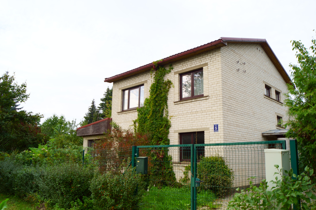 Ķieģeļu māja ar žogu un zaļumiem.