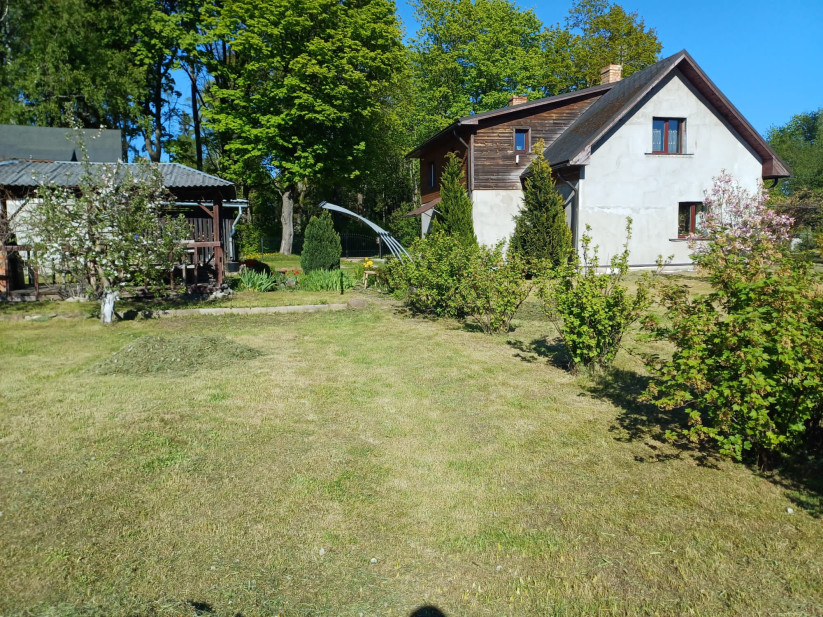 Mājīga divstāvu māja ar zālienu priekšā. 