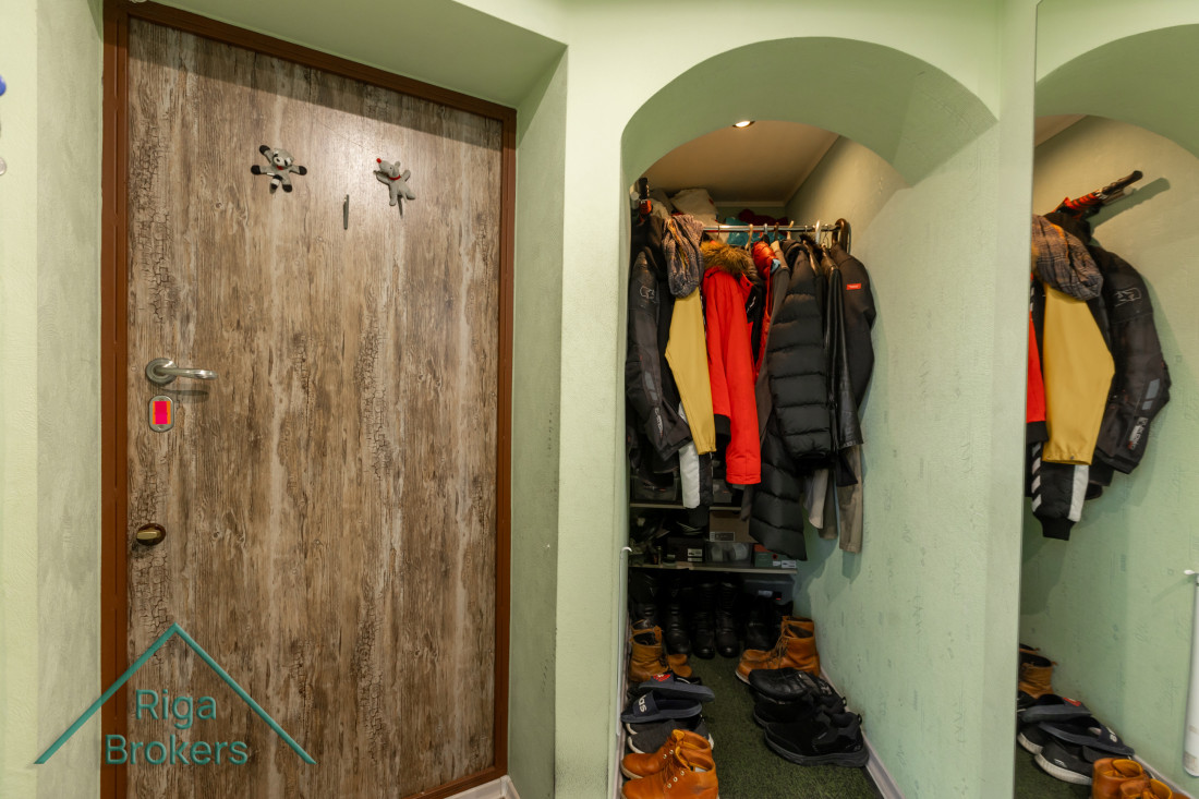 Garderobe ar tumši brūnām durvīm un daudzām jakām.