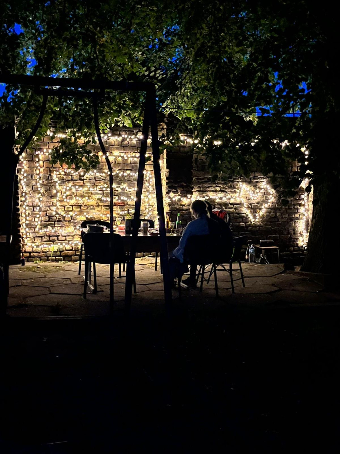 Family dining outdoors by a lit wall.