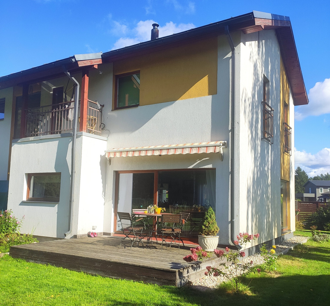 Mājas fasāde ar saulainu terasi un dārzu.