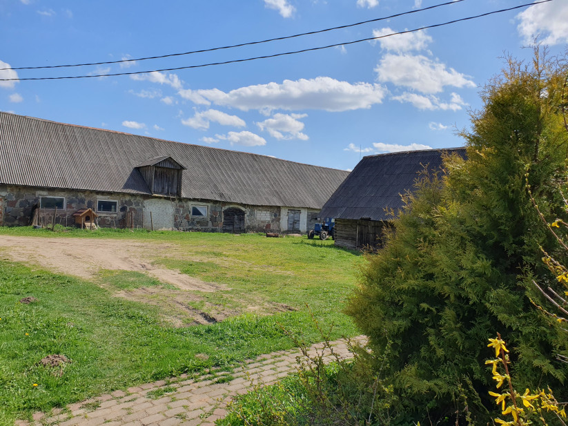 Lielas saimniecības ēkas ar traktoru pagalmā.