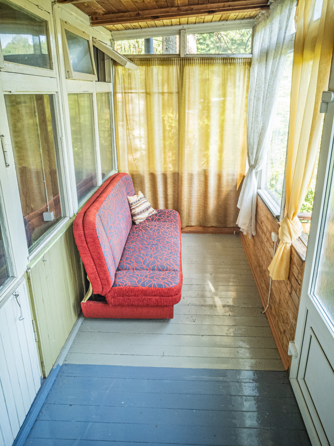 Stiklota veranda ar sarkanu dīvānu.
