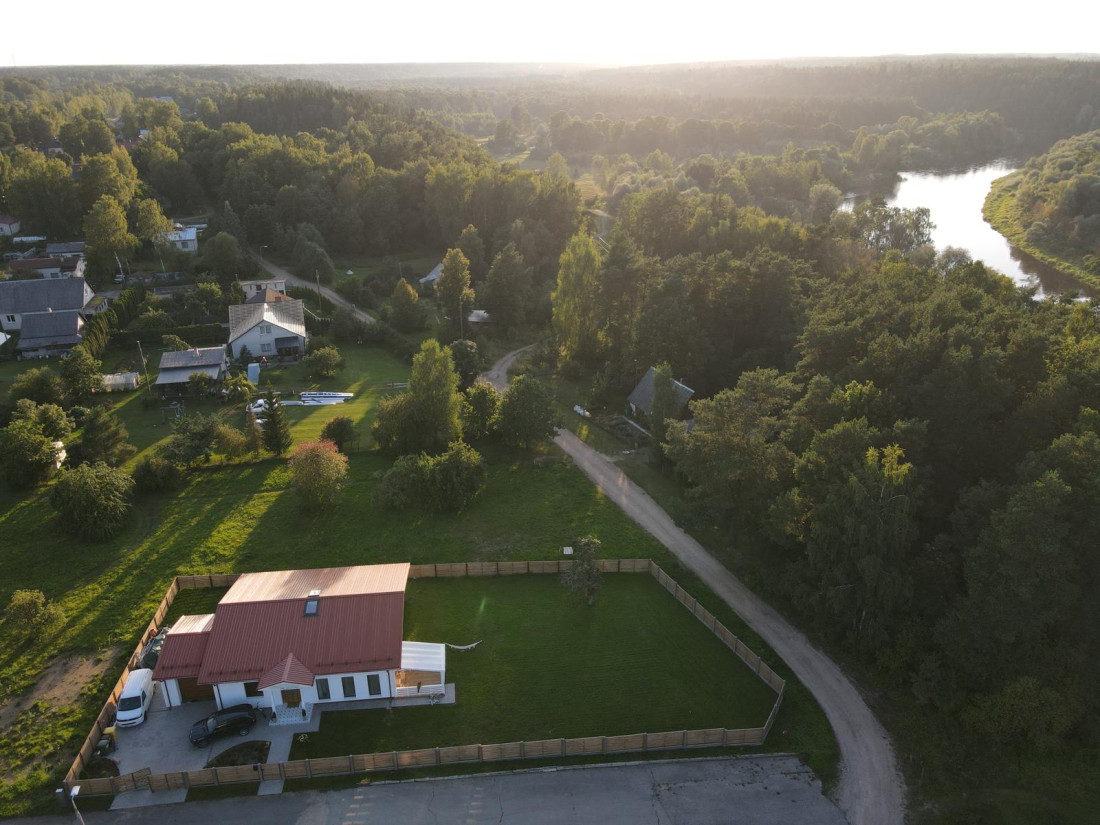 Ainava ar māju un upi fonā.