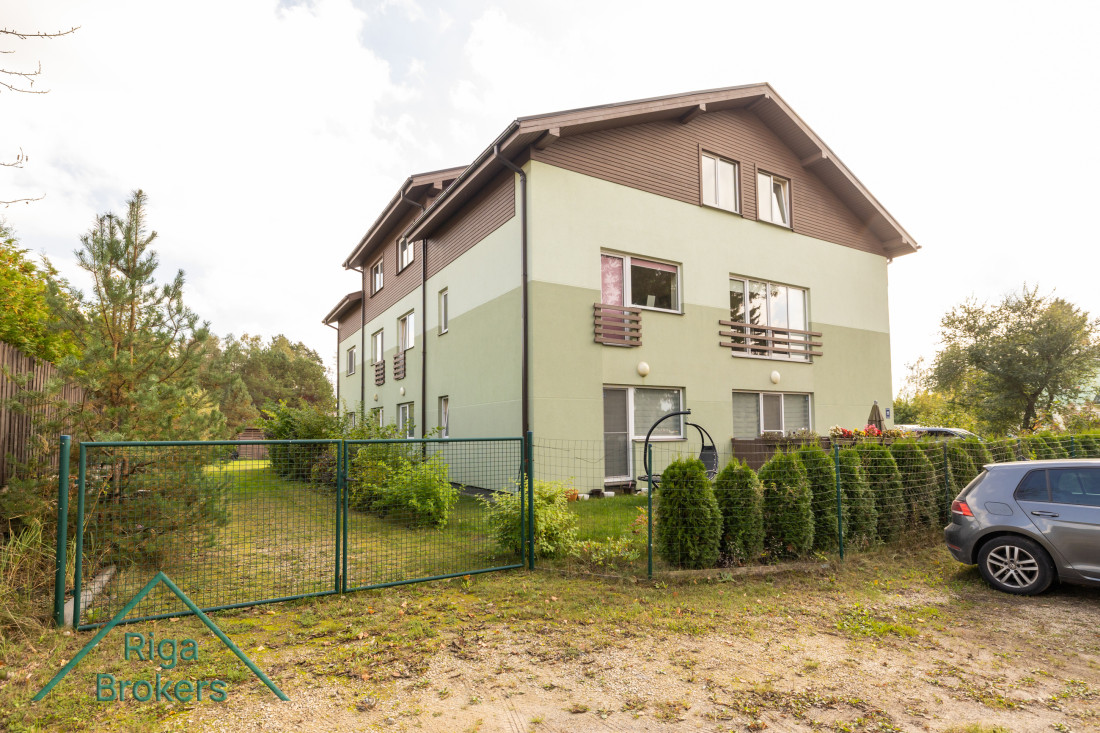 Mājas aizmugure ar zaļu dārzu.