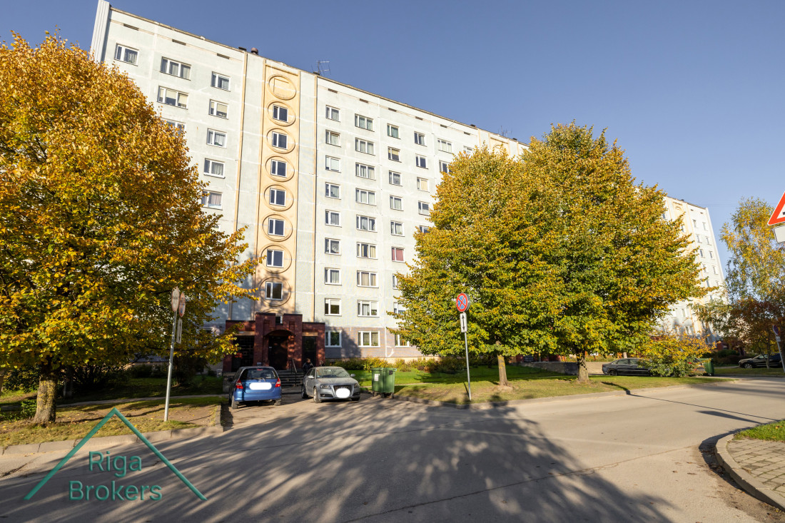 Deviņstāvu ēka ar rudenīgiem kokiem.