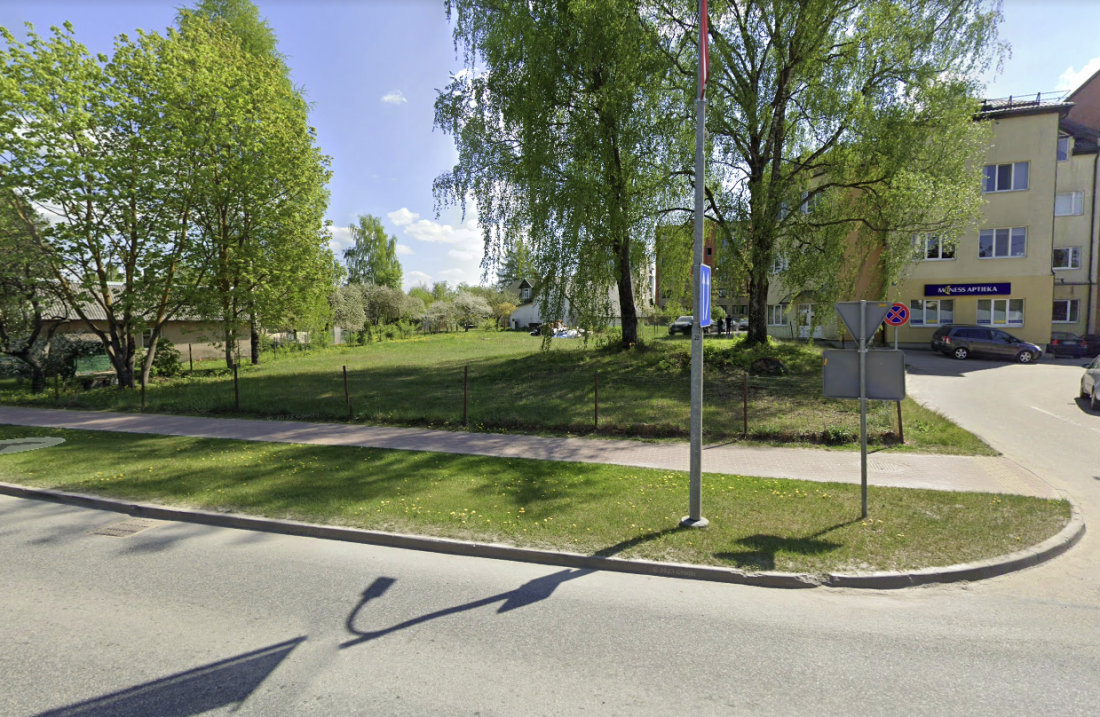 Stūris ar ietvi, kokiem un dzīvokļu ēkām.