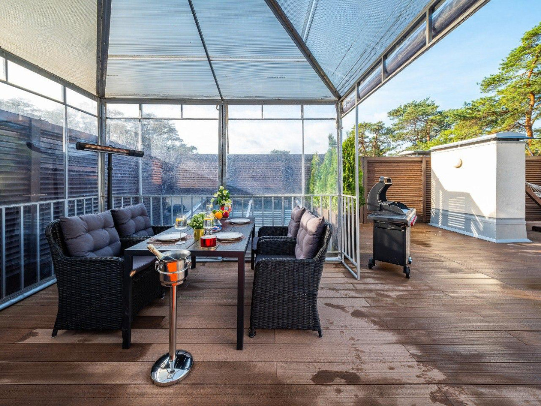 Glass-covered terrace with grill and furniture.