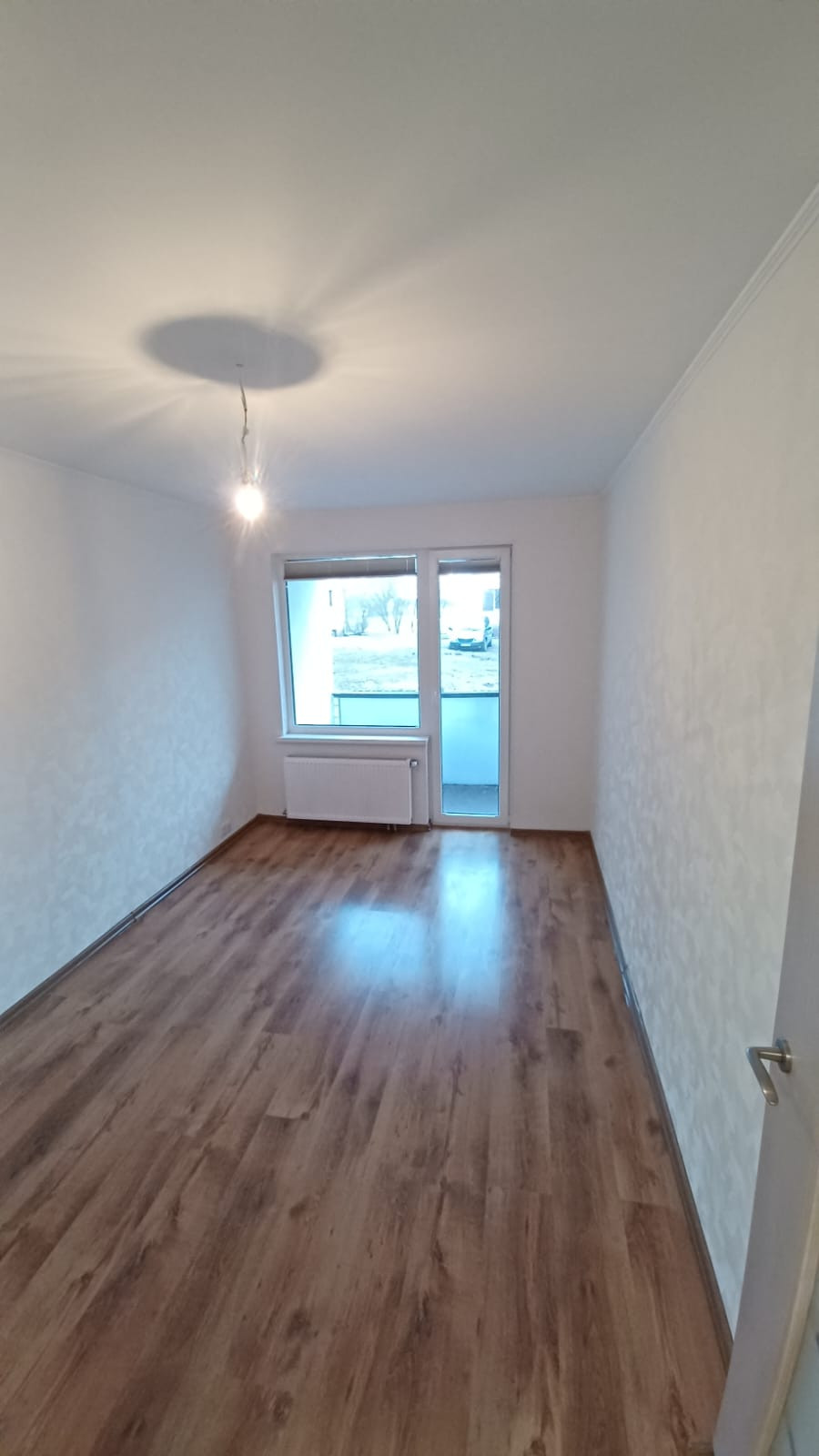 Empty room with laminate flooring and window to the balcony.